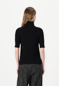 Top tricotat negru cu nervuri, cu guler înalt și mâneci scurte, având un design ajustat care se conturează după corp.