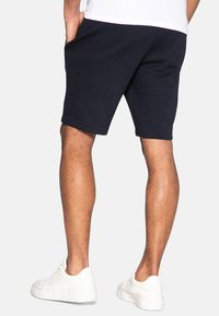 Marineblå bomulds-sportsshorts med sidelommer, ribbet tekstur, skåret over knæet, kombineret med hvide sneakers.