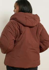 Brązowa kurtka puchowa z dużym kapturem, z pikowanym wzorem i elastycznymi mankietami. Błyszczący, lekki materiał; luźny krótki krój.