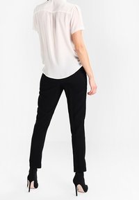 Blusa blanca de manga corta con dobladillo redondeado, pantalones ajustados negros y zapatos de tacón altos negros. Tejido suave, con detalles mínimos.