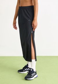 Svart idrottskjol med dragkedja på sidan, tillverkad av ett glatt tyg. I kombination med svarta sneakers och vita ankelsockor.