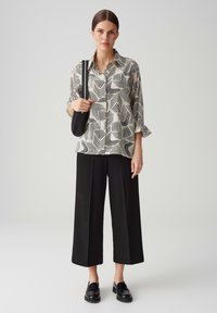 Camicia a maniche lunghe con un motivo astratto bianco e nero, abbinata a pantaloni larghi neri e mocassini neri slip-on.