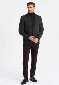 Mörkgrå rutigt blazer över en svart polotröja, parat med vinröda byxor och svarta skor. Slät tygstruktur med skräddarsydd passform.