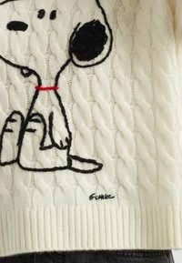 Weißer Strickpullover aus Kabelmuster mit einem bestickten Cartoon-Hund in Schwarz- und Rottönen. Auffällig durch sein strukturiertes Muster und den gerippten Saum.