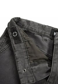 Jeans neri in denim con chiusura a bottone e cerniera, caratterizzati da una texture morbida e dettagli di cucitura sottili. L'etichetta del logo è visibile sulla vita.