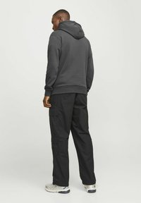 Szara bluza z kapturem, wyposażona w kieszeń z przodu i elastyczne mankiety, zestawiona z czarnymi spodniami cargo posiadającymi wiele bocznych kieszeni i luźny krój.