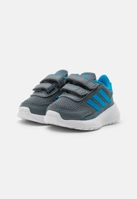 Szare i niebieskie trampki dla malucha z rzepami, oddychająca siateczka na górze, białe podeszwy oraz logo Adidas na palcach i bokach.