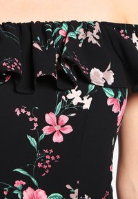 Vestido off-the-shoulder con un escote con volantes. Tejido negro con patrones florales coloridos en rosa, blanco y verde. Textura suave.