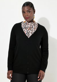 Svart cardigan med V-ringning och knäppning, tillverkad av mjukt tyg. Har långa ärmar och en slät textur, i kombination med en mönstrad topp.