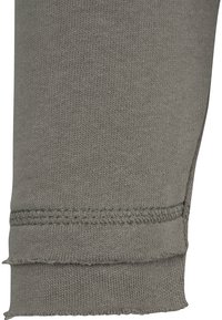 Gros plan sur un tissu tricoté gris avec une double couture et un bord plié, montrant les coutures détaillées et la texture.