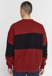 Rød og svart fargeblokkert sweatshirt med rund hals, ribbestrikkede ermer og nederkant. Myk tekstur med avslappet passform.