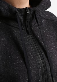 Sweat à capuche noir en tissu texturé parsemé de taches blanches. Doté d'une fermeture éclair intégrale et de cordons de serrage réglables. Matière douce avec une coupe décontractée.