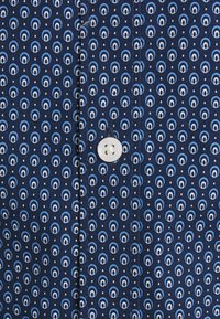 Granatowa koszula z powtarzającym się wzorem małych okręgów w jasnoniebieskim i ciemnoniebieskim kolorze. Posiada białe guziki oraz teksturę materiału.