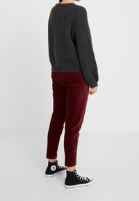 Pull en maille gris, pantalon en velours côtelé rouge et baskets montantes noires. Le pull est texturé, tandis que le pantalon présente des côtes verticales.