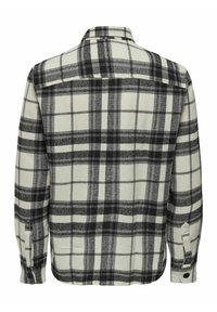 Camisa de cuadros en crema, negro y gris. Presenta mangas largas, puños con botón, patrón de cuadros y un collar. Tejido suave y texturizado.