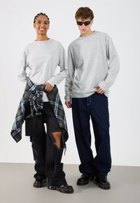 Cămăși gri cu mâneci lungi, pantaloni negri uzați cu margini destrămate, flanel în carouri legat la brâu și încălțăminte neagră. Accesorii minime.