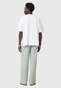 Hvid oversized t-shirt med rund halsudskæring og korte ærmer, parret med lysegrønne vide bukser og brunt fodtøj.