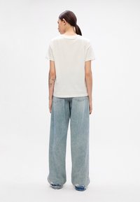 White cotton t-shirt with short sleeves, paired with light blue wide-leg jeans featuring a frayed hem. View from the back.