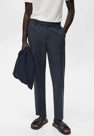 Pantalones de vestir azul marino oscuro con corte recto, cierre de botón y bolsillos laterales, combinados con una camisa blanca y una chaqueta oscura.
