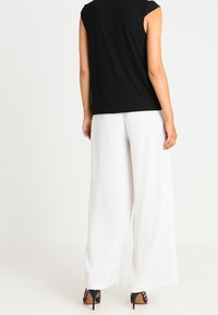 Top negro de mangas cortas combinado con pantalones anchos blancos. Los pantalones tienen una textura suave y un diseño largo hasta el suelo. Se pueden ver unos zapatos de tacón alto negros.