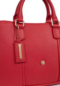 Borsa a tracolla in pelle rossa con texture a ciottoli, manici doppi, dettagli in metallo dorato e un'etichetta rettangolare attaccata da una catena. Presenta una chiusura a scatto.