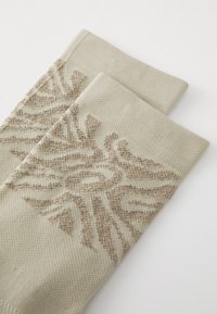 Chaussettes en tricot beige avec un motif texturé dans des nuances de brun. Comprend une bordure lisse et une zone de renfort au niveau des orteils.
