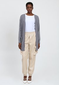 Lichtgrijze cardigan, wit t-shirt en crèmekleurige broek met elastische tailleband. De hakken hebben een spitse neus en een decoratieve band.