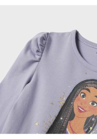 Chemise manches longues violet clair avec un graphisme de personnage aux accents dorés. Les manches bouffantes ajoutent de la texture, avec un col rond et un tissu doux.