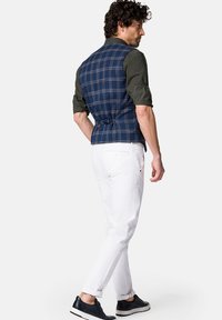 Granatowa kamizelka w kratę o dopasowanym kroju, zestawiona z ciemnozieloną koszulą i białymi spodniami. Stylizację dopełniają czarne sneakersy.