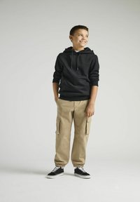 Schwarzer Baumwoll-Hoodie mit einer Fronttasche und Kordeln, kombiniert mit beigen Cargo-Hosen mit seitlichen Taschen und schwarzen Sneakers.