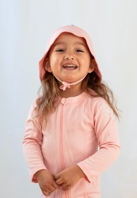 Rosa solhatt med bred skärm och hakrem, bärs tillsammans med en matchande långärmad baddräkt som har dragkedja fram och texturerat tyg.