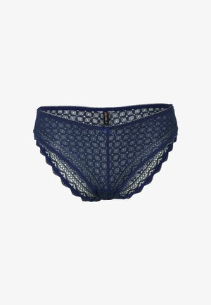 Perizoma in pizzo blu navy con motivo a diamante, bordi ondulati e un fiocco decorativo centrale. Etichetta con il nome del marchio visibile.