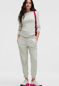 Lichtgrijze langemouwen top gecombineerd met bijpassende joggers. De joggers hebben zijzakken en een trekkoord in de taille. Witte schoenen met roze accenten.