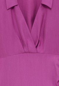 V-pääntieltä ja taitetulta kauluksella varustettu violetti mekko. Kangas näyttää sileältä, siinä on hienovarainen kiilto, ja se laskeutuu pehmeästi vyötärön ympärille.