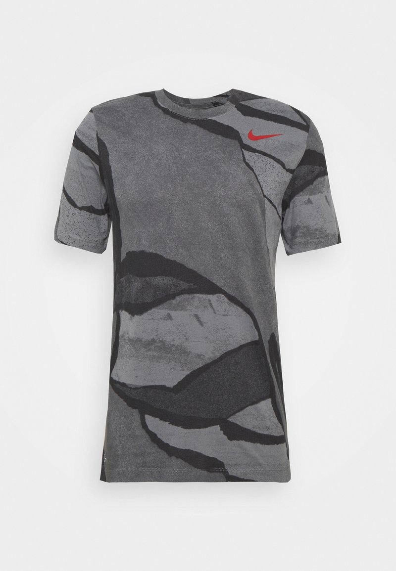 Camiseta gris de manga corta con un patrón abstracto en negro y gris oscuro. Presenta un prominente logo de Nike en rojo en el hombro superior izquierdo.