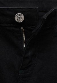 Mustat denim-farkut, joissa on metallinen napitus, vetoketju ja hienot tikkaustiedot vyötärön ja taskujen ympärillä. Sileä kankaan rakenne.