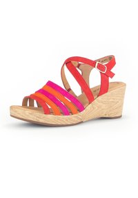 Sandale compensée avec une base en bois naturel, présentant des brides en daim rayées rouge, rose et orange, ainsi qu'une sangle de cheville avec une boucle.