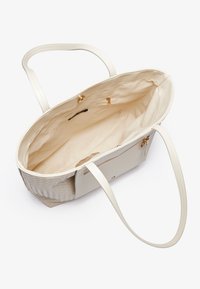 Stor beige tote taske med vævet tekstur og glatte syntetiske sider. Har to lange håndtag, et rummeligt interiør med stofforing og lynlås lommer.