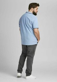 Lichtblauwe polo met kraag, donker accent, gecombineerd met donkergrijze jeans en witte sneakers, bekeken vanuit de achterkant.