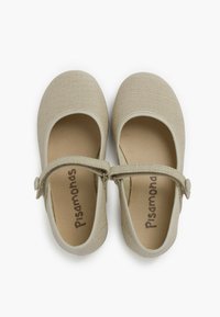 Beige plátěné boty typu Mary Jane s kulatou špičkou, nastavovacím popruhem a měkkými béžovými vložkami. Texturovaný povrch a logo vytištěné uvnitř.