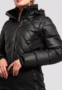 Zwarte geïsoleerde jas met een gewatteerd patroon, capuchon en een rits aan de voorkant. Heeft een slank ontwerp en contrasterende zwarte stofaccenten.
