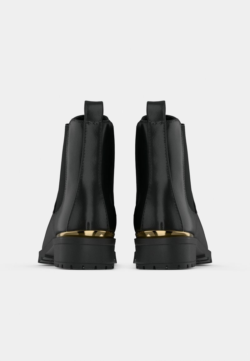 Une paire de bottes Chelsea noires avec des semelles épaisses et des accents métalliques dorés à l'arrière des talons, présentée de l'arrière sur un fond uni.