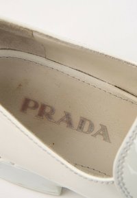 Gros plan de l'intérieur d'une chaussure en cuir blanc montrant le logo Prada estompé sur la semelle intérieure.