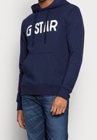 Sudadera azul marino con un bolsillo delantero, capucha con cordón y gran logo blanco de G-Star. Tejido suave con puños y dobladillo acanalados.