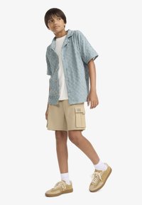 Ανοιχτό μπλε κοντομάνικο πουκάμισο με υφημένο σχέδιο καρό, συνδυασμένο με μπεζ cargo σορτς και ταμπά αθλητικά παπούτσια με κρεμ σόλες.