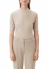 Beżowy prążkowany top z wysokim kołnierzem i krótkimi rękawami, w zestawie z beżowymi spodniami. Tkanina jest gładka i dopasowana, z delikatnymi pionowymi liniami.