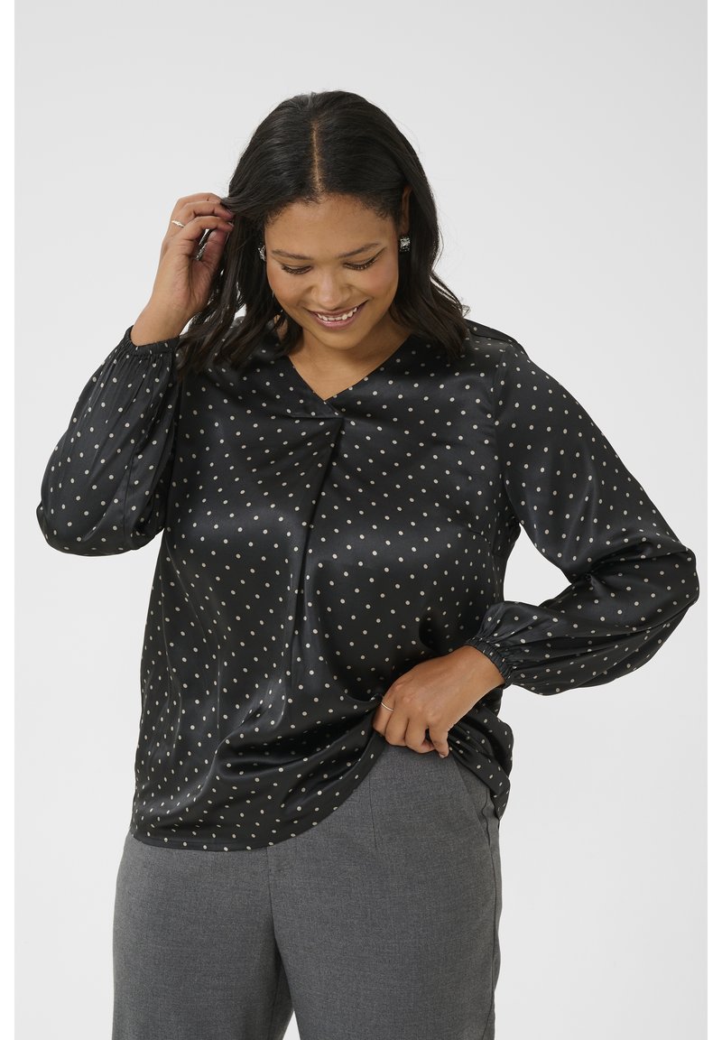 Blouse en satin noir avec des pois dorés, décolleté en V et manches froncées. Son éclat doux et sa coupe drapée créent une silhouette fluide.