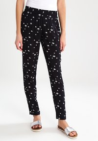 Černé kalhoty s bílými vzory ptáků, elastický pas, tapered střih, lehká látka, spárované se stříbrnými klouzacími sandály.