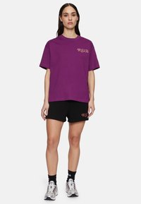 Paarse katoenen T-shirt met korte mouwen en het "R.S.V.P."-logo. Gecombineerd met zwarte shorts met een bijpassend geborduurd logo. Witte sneakers.
