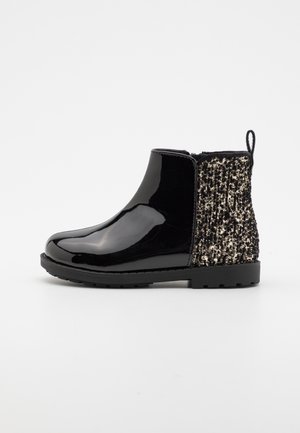 Stivale alla caviglia in pelle nera lucida con tessuto texturizzato dorato e nero sul retro, suola piatta e linguetta per una facile calzata.